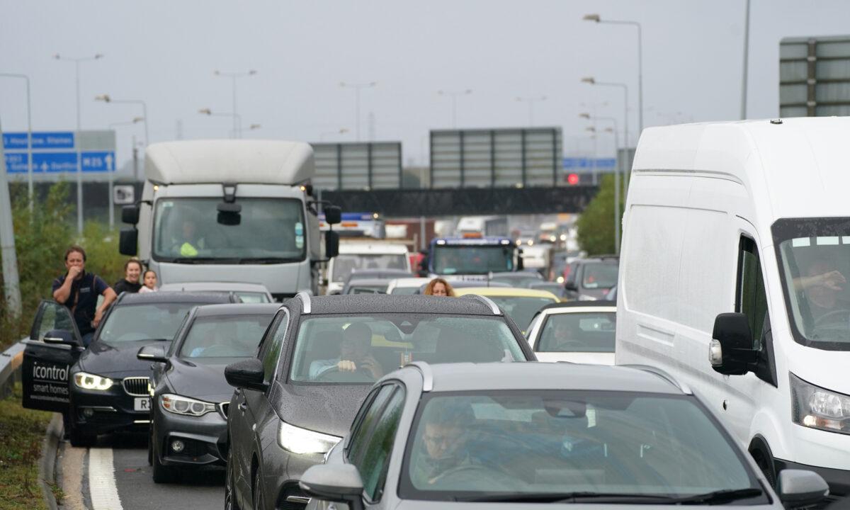 Drivers stand watching from their cars as traffic is halted during a roadblock by protesters from Insulate Britain at a roundabout leading from the M25 motorway to Heathrow Airport in London on Sept. 27, 2021. (Steve Parsons/PA)