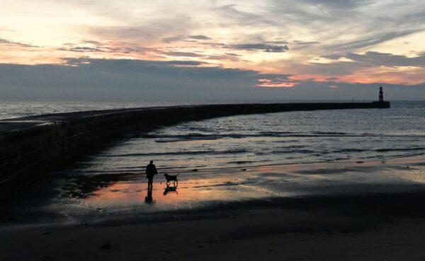 A dogwalker walks along the beach at sunrise at Seaham Harbour in Seaham, north east England on Oct. 7, 2021. (Paul Ellis/AFP via Getty Images)