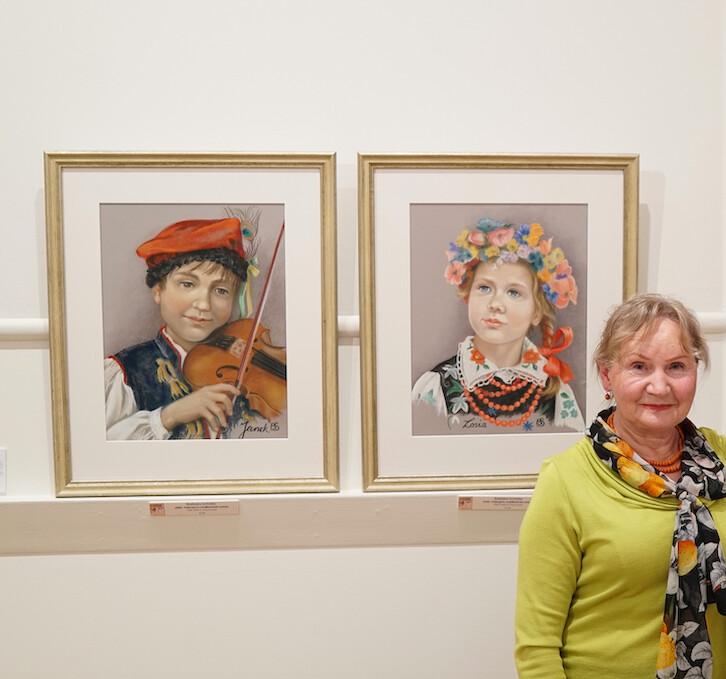 Barbara Schafer next to her pastel paintings of Polish children in traditional costume at a Polish art exhibition titled "Roots" in Melbourne, Australia, in 2018. (Courtesy of Barbara Schafer)