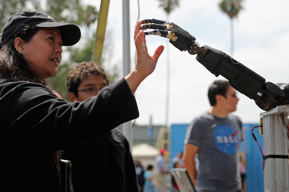 A woman reaches to touch a robotic arm developed by the Johns Hopkins University Applied Physics Laboratory on display at the Defense Advanced Research Projects Agency (DARPA, the Pentagon's science research group) Robotics Challenge Expo at the Fairplex in Pomona, Calif., on June 6, 2015. (Chip Somodevilla/Getty Images)