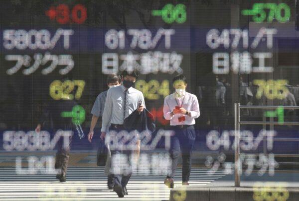 People wearing protective masks, amid the CCP virus outbreak, are reflected on an electronic board displaying Japan's stock prices outside a brokerage in Tokyo on Oct. 5, 2021. (Kim Kyung-Hoon/Reuters)