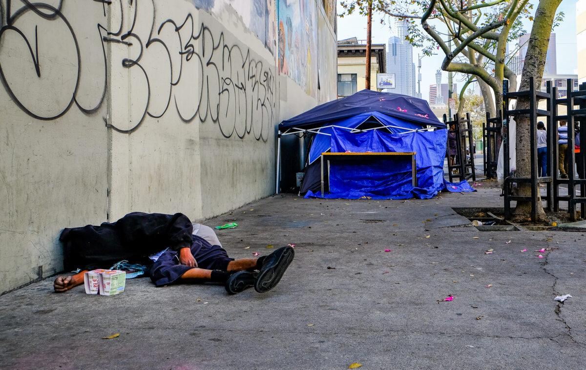 A homeless man sleeps near tents in a file photo in downtown Los Angeles on Nov. 18, 2018. (John Fredricks/The Epoch Times)