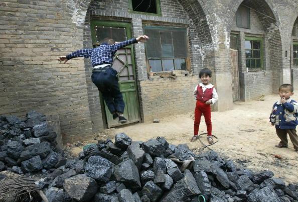 Children play outside their cave-style homes beside a pile of coal, 26 May 2004 in Xiaoyi, in the hills outside of Taiyuan in northern China's Shanxi province, the country's biggest coal producing province. (FREDERIC J. BROWN/AFP via Getty Images)