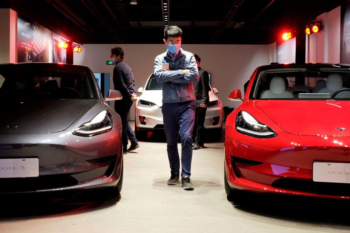 A man wearing a face mask following the coronavirus disease outbreak walks past Tesla Model 3 sedans and Tesla Model X sport utility vehicle at a new Tesla showroom in Shanghai, on May 8, 2020. (Yilei Sun/Reuters)