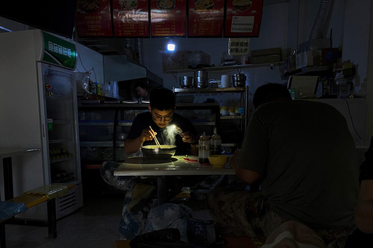 A man uses his smartphone flashlight to light up his bowl of noodles as he eats his breakfast at a restaurant during a blackout in Shenyang in northeastern China's Liaoning Province, on Sept. 29, 2021. (Olivia Zhang/AP Photo)