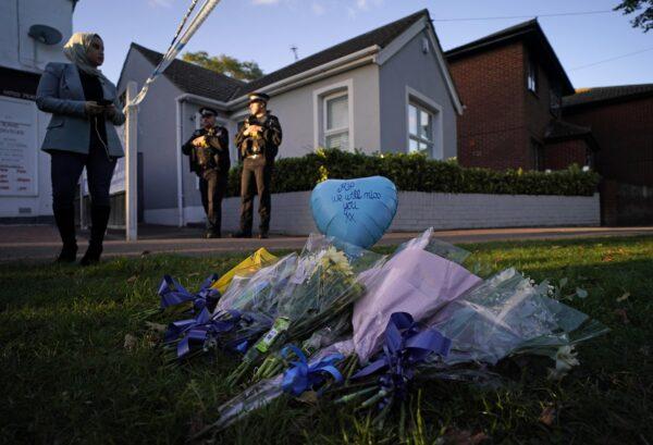 Floral tributes can be seen as police officers block one of the roads leading to the Belfairs Methodist Church in Eastwood Road North, where British Conservative lawmaker David Amess has died after being stabbed at a constituency surgery, in Leigh-on-Sea, Essex, England, on Oct. 15, 2021. (Alberto Pezzali/AP Photo)