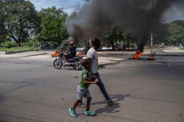A man and a child walk by burning tires on a street in Port-au-Prince, Haiti, on Oct. 17, 2021.(Joseph Odelyn/AP Photo)