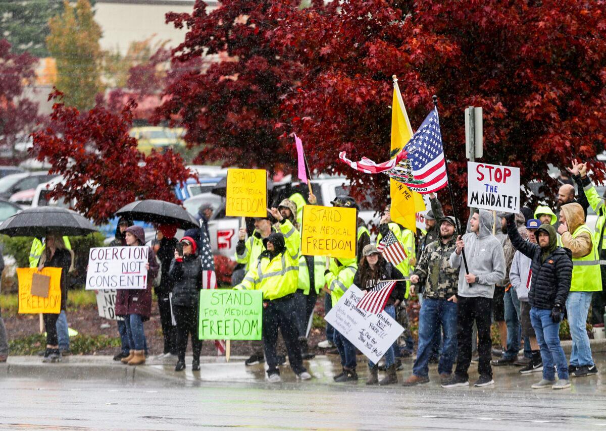 Boeing employees and others wave to passing traffic in the rain as they protest the company's COVID-19 vaccine mandate, outside the Boeing facility in Everett, Wash., on Oct. 15, 2021. (Lindsey Wasson/Reuters)