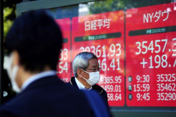 A man wearing a protective mask looks at an electronic stock board showing Japan's Nikkei 225 (C) and New York Dow indexes at a securities firm in Tokyo, Japan on Oct. 20, 2021. (Eugene Hoshiko/AP Photo)