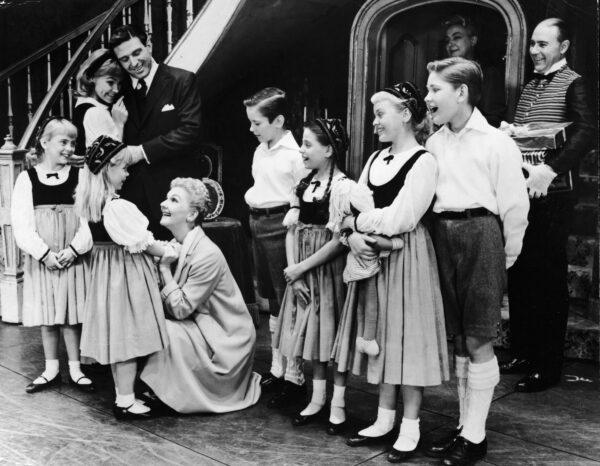 American actress Mary Martin kneels to hear some news from one of the von Trapp children in a scene from 'The Sound of Music' at the Lunt-Fontanne Theatre in New York in late 1950s. Also watching is Austrian actor Theodore Bikel (in suit at left), who plays Baron von Trapp, and Austrian actor Kurt Kasznar (far right). (Authenticated News/Getty Images)