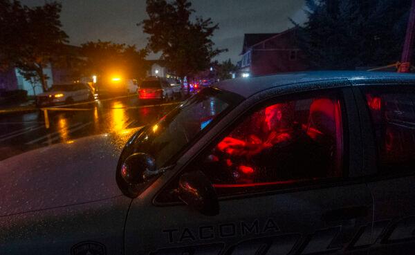 A Tacoma police officer works in his squad car while blocking access to a street where four people were shot and killed, in Tacoma, Wash., on Oct. 21, 2021. (Drew Perine/The News Tribune via AP)