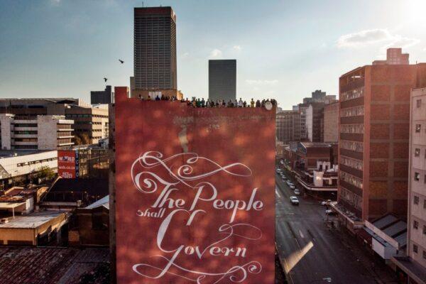 This aerial view shows residents gathering on a roof of a building, with artwork on the side of the building by South African artist Faith XLVII in Johannesburg, South Africa, on April 22, 2020. (Macro Longari/AFP via Getty Images)