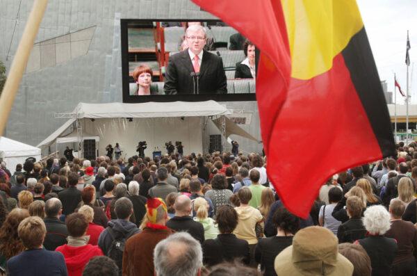An Aboriginal flag waves in front of the giant television screen as thousands gather in Melbourne's Federation Square, Australia, on Feb. 13, 2008, to listen to Prime Minister Kevin Rudd deliver a historic apology in parliament to the Aboriginal people for injustices committed over two centuries of white settlement. (William West/AFP via Getty Images)