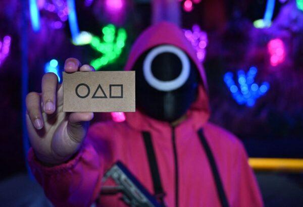 A waiter dressed in an outfit from the Netflix series Squid Game holds a card while playing a game to attract customers at a cafe in Jakarta on Oct. 19, 2021. (Photo by Adek Berry/AFP via Getty Images)