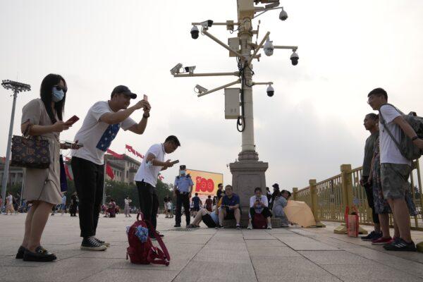 Visitors take photos near surveillance cameras on Tiananmen Square in Beijing as a policeman stands watch nearby, on July 15, 2021. (Ng Han Guan/AP Photo)