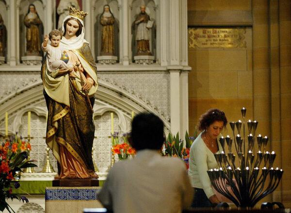 A worshipper lights a candle while another prays inside St Mary's Cathedral in Sydney, Australia, on April 1, 2005. (Rob Elliot/AFP via Getty Images)