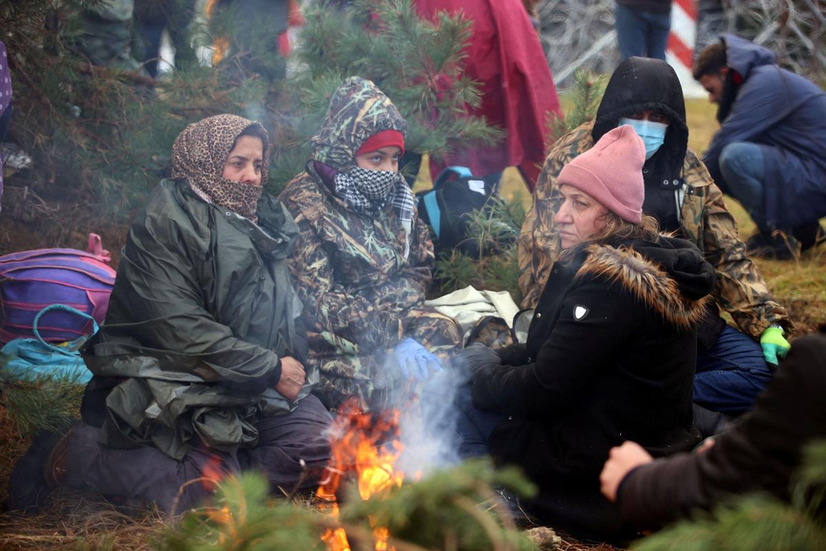 Migrants sit around a fire near a barbed wire fence in an attempt to cross the border with Poland in the Grodno region, Belarus, on Nov. 8, 2021. (Leonid Scheglov/BelTA/Handout via Reuters)