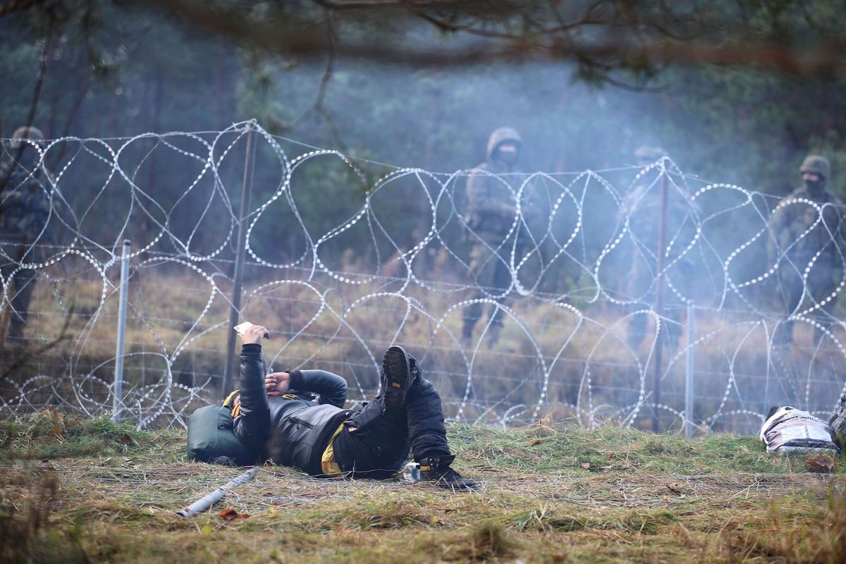 A migrant lies on the ground next to a barbed wire fence on the Belarusian-Polish border in the Grodno region, Belarus, on Nov. 8, 2021. (Leonid Scheglov/BelTA/Handout via Reuters)
