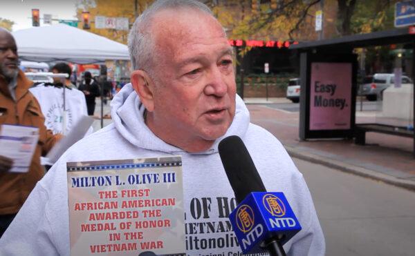 Vietnam War veteran Robert Toporek, the author of the book “Milton L. Olive III: The First African American Awarded the Medal of Honor in the Vietnam War,” holds his book at the 7th Annual Veterans Parade in Philadelphia, Pa., on Nov. 7, 2021. (Screenshot via NTD)
