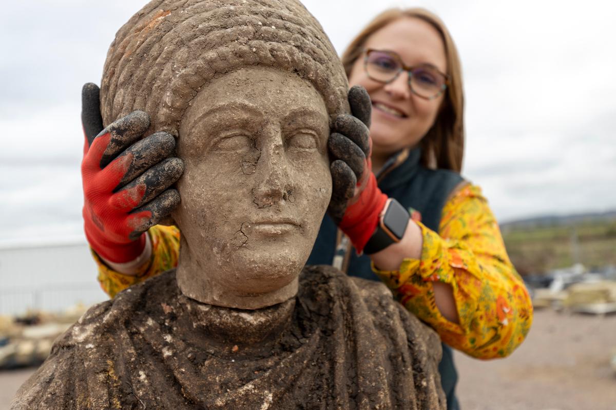 Dr. Rachel Wood, lead archaeologist contractor with Fusion JV, holds up the statue head of a woman from the Roman age, depicted with ornate braided hair or headdress. (Courtesy of <a href="https://mediacentre.hs2.org.uk/news/incredible-rare-roman-statues-found-in-hs2-dig">HS2</a>)