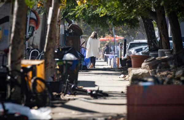 A woman walks down a sidewalk passing a homeless encampment in Venice Beach, Calif., on Nov. 10, 2021. (John Fredricks/The Epoch Times)