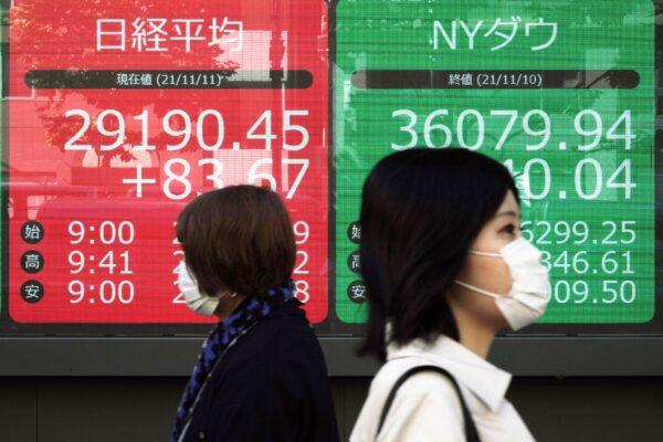 Women wearing protective masks walk Japan's Nikkei 225 and New York Dow indexes at a securities firm in Tokyo on Nov. 11, 2021. (Eugene Hoshiko/AP Photo)