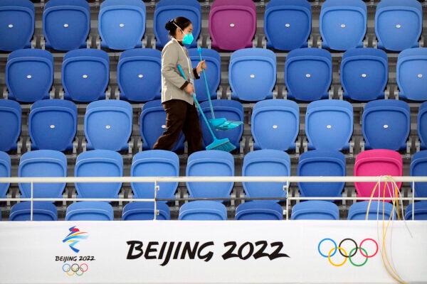 A maintenance worker wearing a face mask walks through an empty section of spectator stands near a logo for the Beijing 2022 Winter Olympics during the Speed Skating China Open, a test event for the 2022 Winter Olympics, at the National Speed Skating Oval in Beijing, on Oct. 10, 2021. (Mark Schiefelbein/AP Photo)