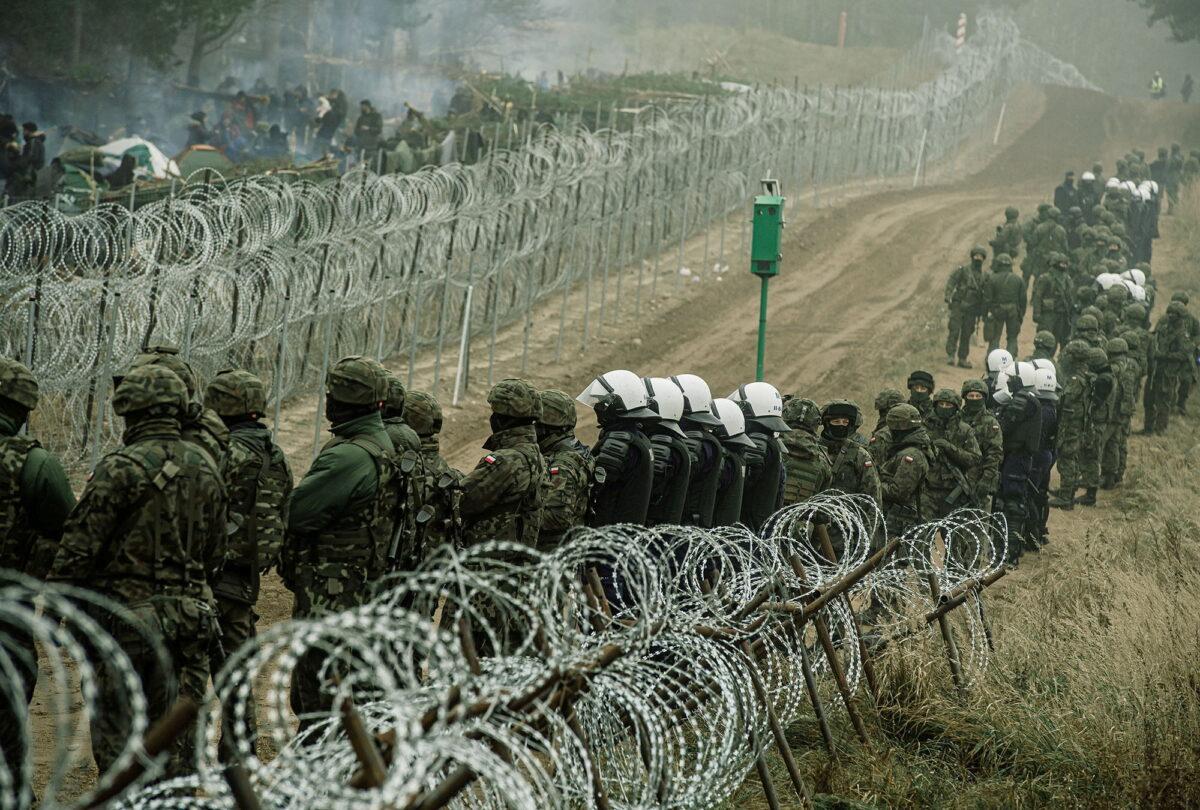 In this photograph released by the Territorial Defence Forces, Polish soldiers and police watch illegal immigrants at the Poland/Belarus border near Kuznica, Poland, on Nov. 12, 2021. (Irek Dorozanski/DWOT/Handout via Reuters)
