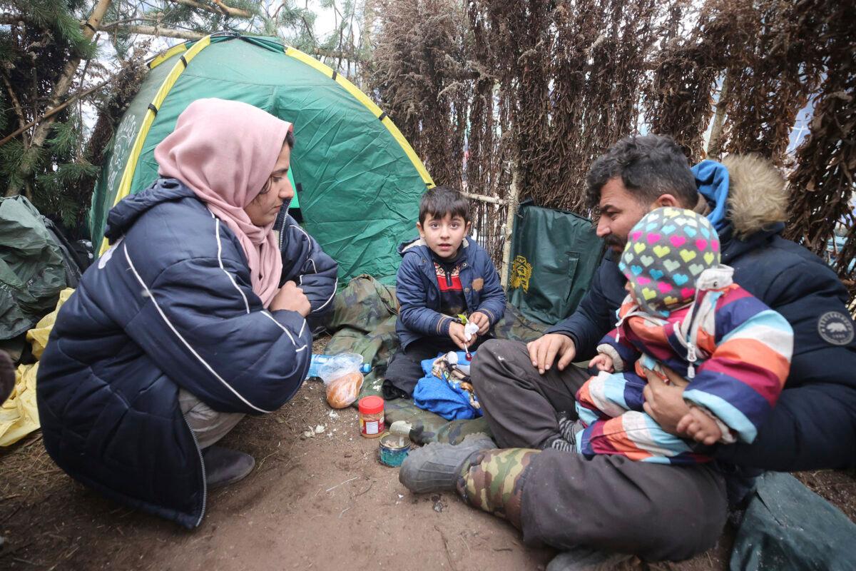 A family eat at a tent camp as migrants gather at the Belarus-Poland border near Grodno, Belarus, Saturday, Nov. 13, 2021. (Leonid Shcheglov/BelTA pool photo via AP)