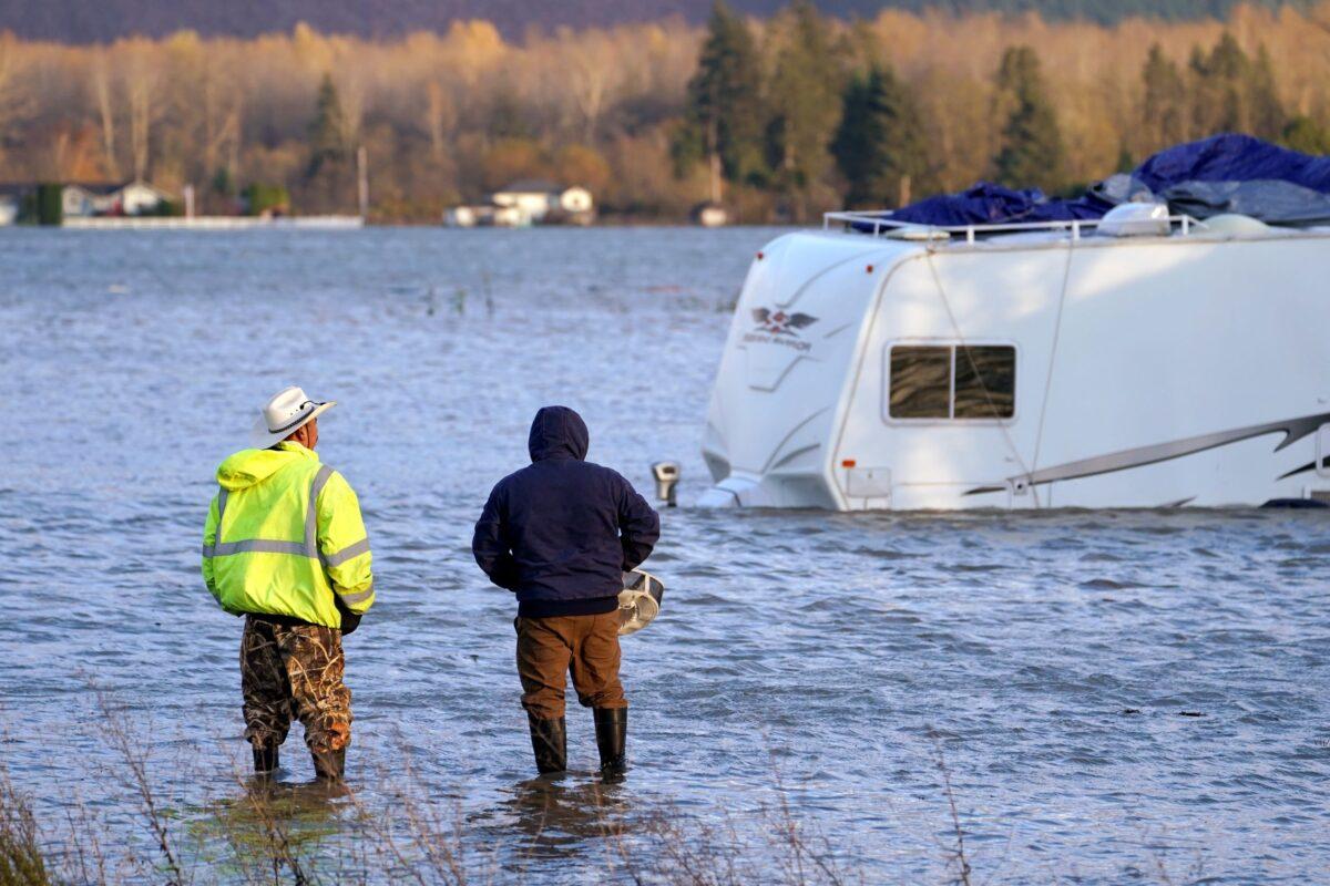 Two men stand in the flooded Skagit River and look across at an RV, in Sedro-Woolley, Wash., on Nov. 15, 2021. (Elaine Thompson/AP Photo)