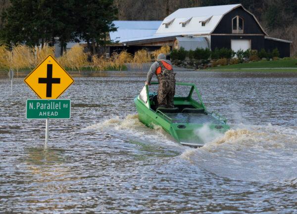 A man drives a boat down a flooded road in Chilliwack, B.C., on Nov. 16, 2021. (The Canadian Press/Jonathan Hayward)