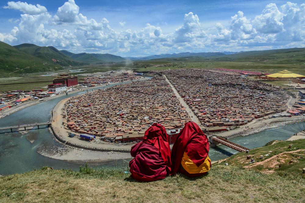 Tibetan monks sitting on the hill and looking at Yarchen Gar Tibetan Buddhist monastery in Sichuan, China. (Phuong D. Nguyen/Shutterstock)