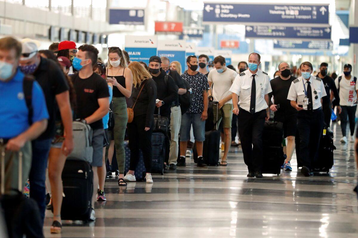 Two airplane pilots pass by a line of passengers while waiting at a security check-in line at O'Hare International Airport in Chicago, Ill., on July 1, 2021. (Shafkat Anowar/AP Photo)