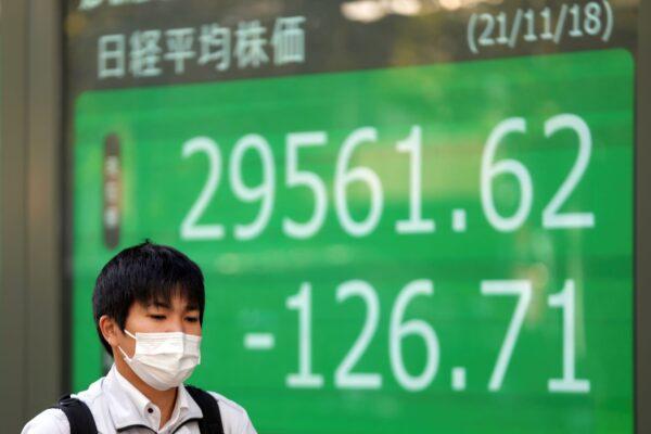 A man wearing a protective mask walks near an electronic stock board showing Japan's Nikkei 225 index at a securities firm, in Tokyo on Nov. 18, 2021. (Eugene Hoshiko/AP Photo)