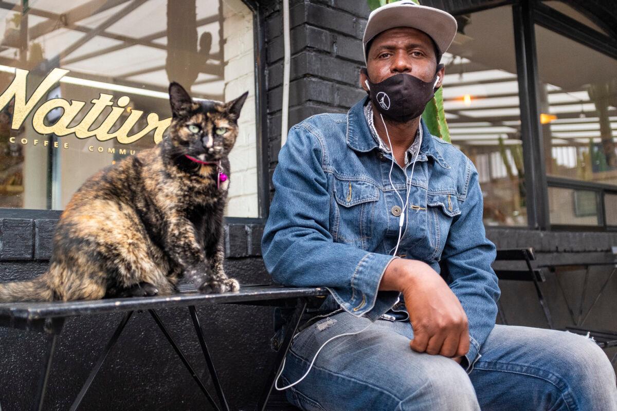 Haitian pastor Fritznel Merite sits next to a cat at the Nativo Coffee Community in Tijuana, Mexico, on Nov. 6, 2021. He also works in a factory to send money home to family in Port au Prince aside from leading a Baptist congregation. (John Fredricks/The Epoch Times)