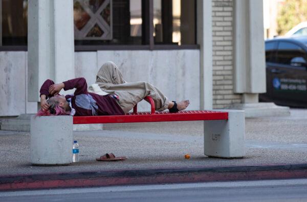A homeless woman lays at a bus stop in Long Beach, Calif., on Oct. 27, 2021. (John Fredricks/The Epoch Times)