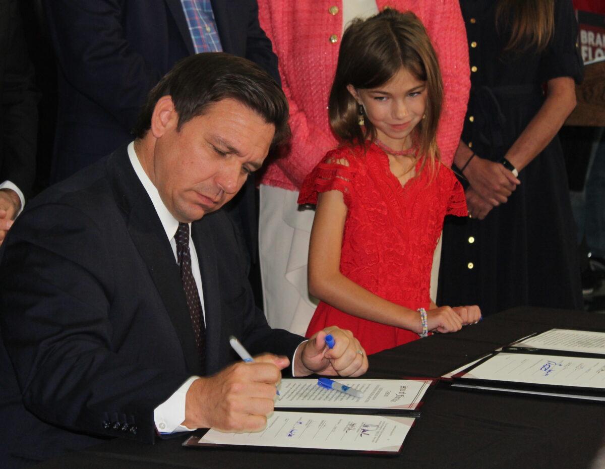 Florida Governor Ron DeSantis signs bills into law as second grader Fiona LaShells looks on, on Nov. 18, 2021. (Jann Falkenstern, The Epoch Times)