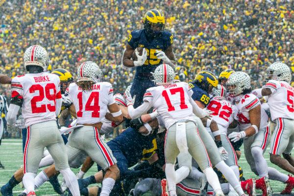 Michigan running back Hassan Haskins (25) leaps over Ohio State defenders for a touchdown in the second quarter of an NCAA college football game in Ann Arbor, Mich., on Nov. 27, 2021. (Tony Ding/ AP Photo)