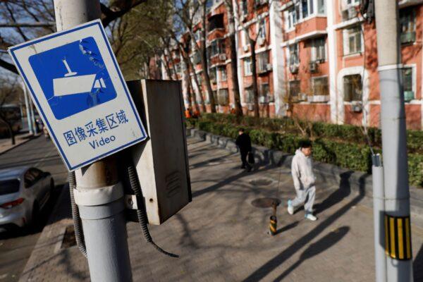 A sign noting that the area is under video surveillance is pictured on a pole while people walk on a street in Beijing on Nov. 25, 2021. (Carlos Garcia Rawlins/Reuters)