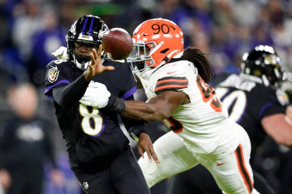Baltimore Ravens quarterback Lamar Jackson (8) pitches the ball to running back Devonta Freeman, not visible, as Cleveland Browns defensive end Jadeveon Clowney (90) applies pressure during the first half of an NFL football game, in Baltimore, on Nov. 28, 2021. (Gail Burton/AP Photo)