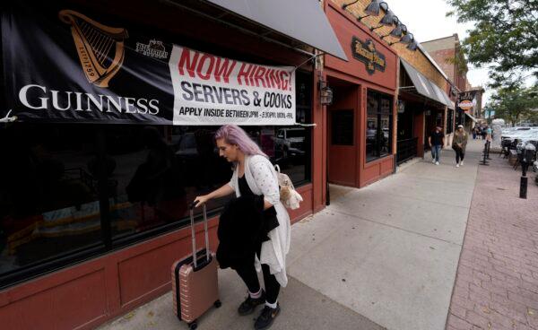 A traveler wheels her baggage past a now hiring sign outside a bar and restaurant, in Sioux Falls, S.D., on Oct. 9, 2021. (David Zalubowski/AP Photo)