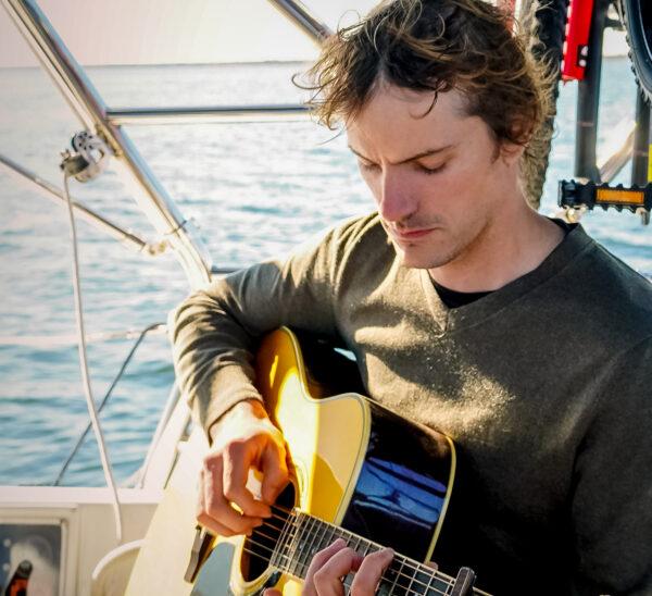 Alex Wynn strumming his guitar while aboard the sailboat off the coast of South Carolina, in December 2021. (Kristi Wynn)