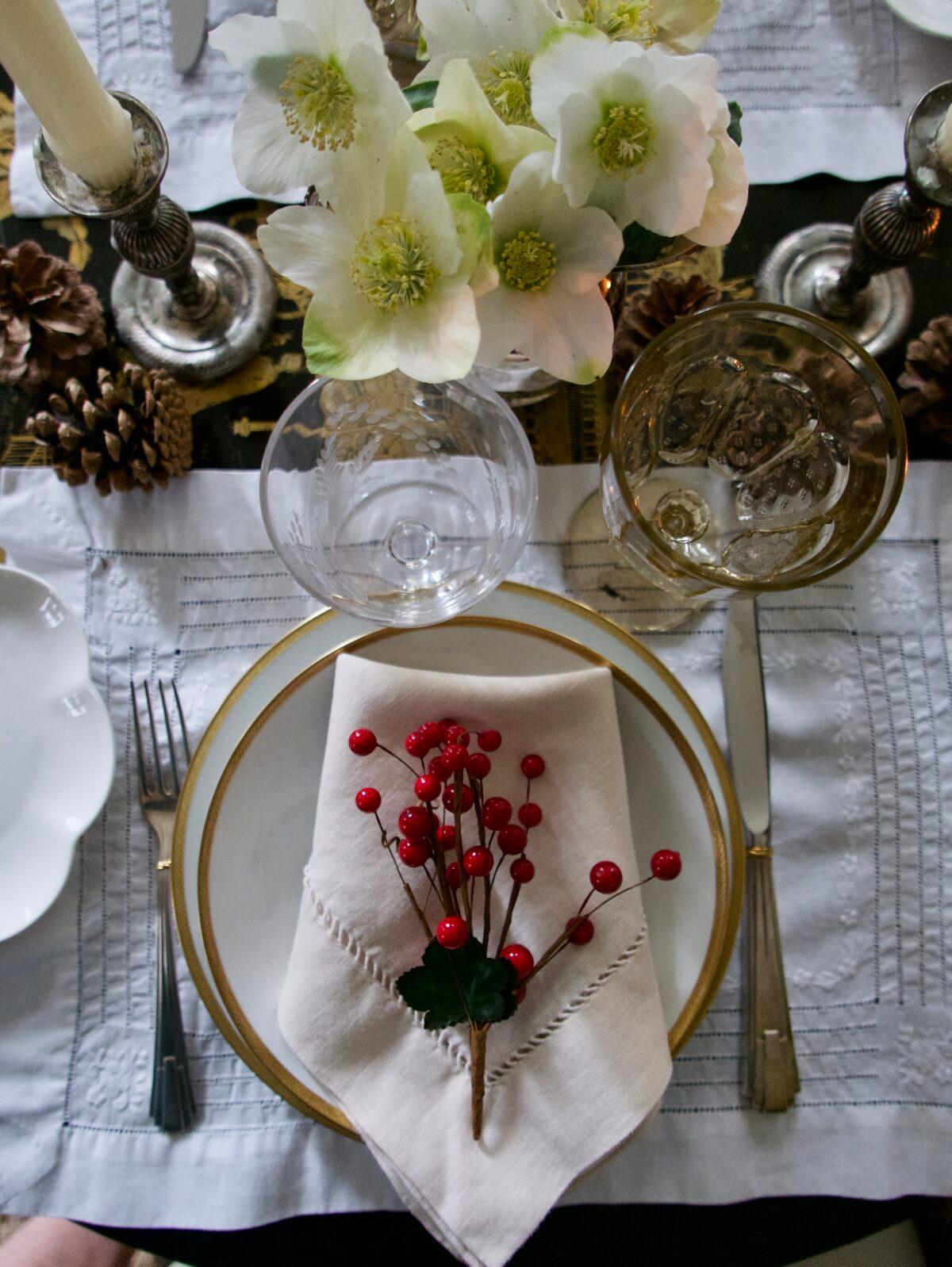 On the table: Pinecones and red berries play with white hellebores, silver and gold add a bit of glimmer and glow, and white linens add an understated elegance. (Victoria de la Maza)