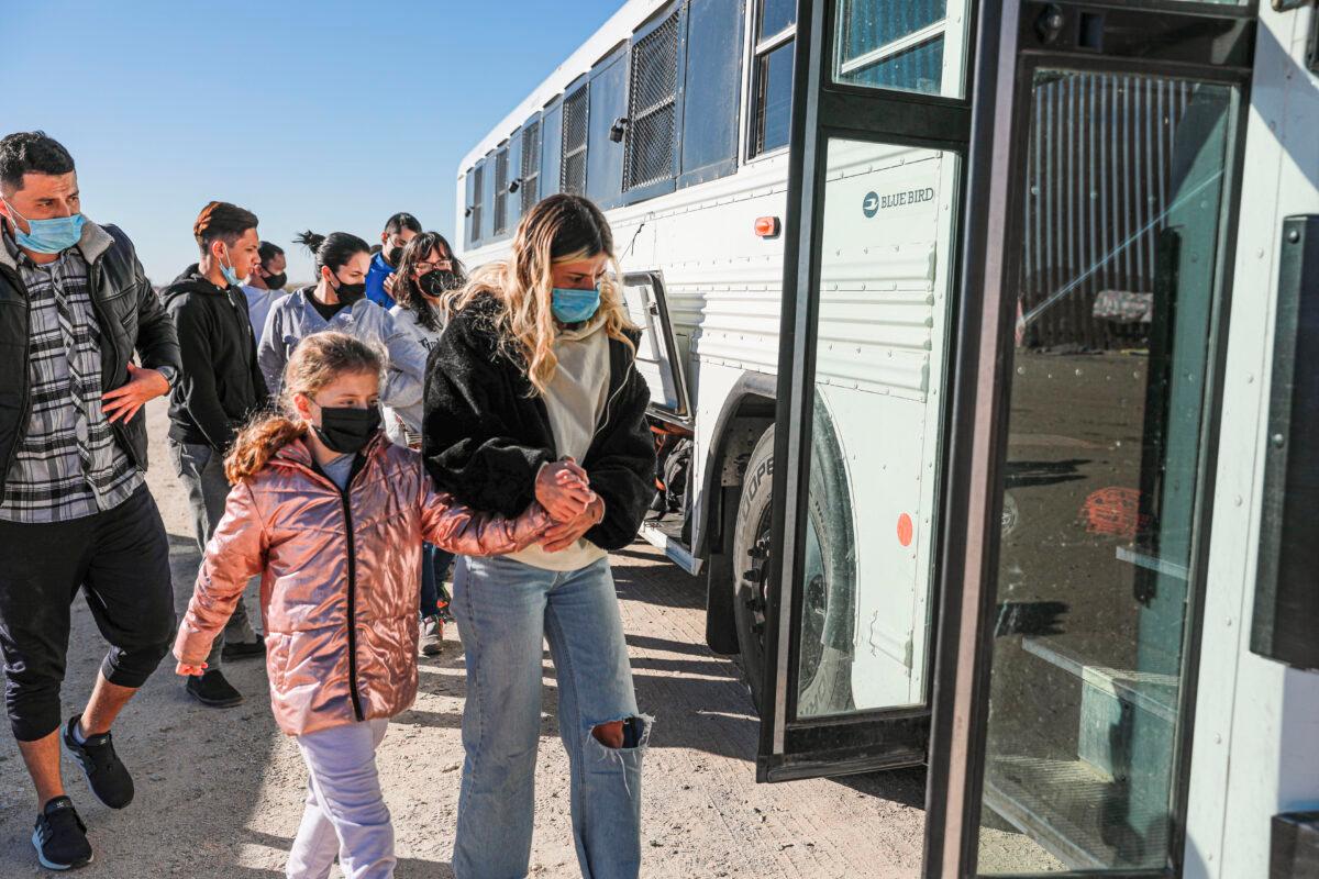 Illegal immigrants who have gathered by the border wall board a bus going to the Border Patrol station for processing in Yuma, Ariz., on Dec. 10, 2021. (Charlotte Cuthbertson/The Epoch Times)