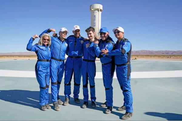 (L-R) Blue Origin's latest space passengers Laura Shepard Churchley, Dylan Taylor, Michael Strahan, Cameron Bess, Lane Bess, and Evan Dick pose for a photo in front of the booster rocket at the spaceport near Van Horn, Texas, on Dec. 11, 2021. (LM Otero/AP Photo)