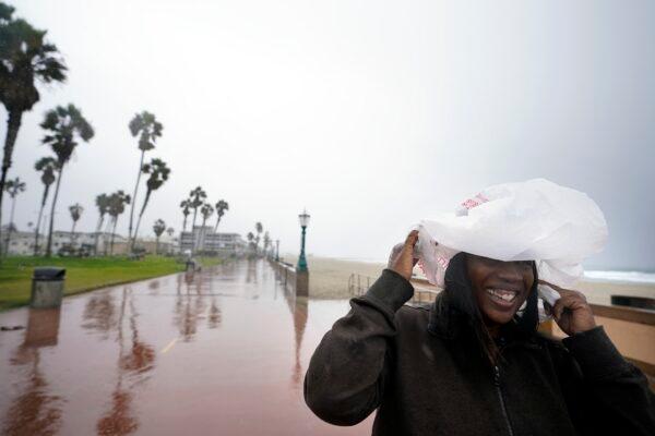 Michelle Jones covers her head with a bag as she watches large waves along Mission Beach in San Diego, on Dec. 14, 2021. (Gregory Bull/AP Photo)