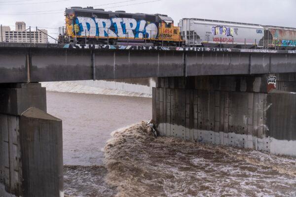A cargo train passes over a bridge where a submerged vehicle is wedged against the bridge's pillar in the surging Los Angeles River making it difficult for firefighters to access it in Los Angeles, on Dec. 14, 2021. (Damian Dovarganes/AP Photo)