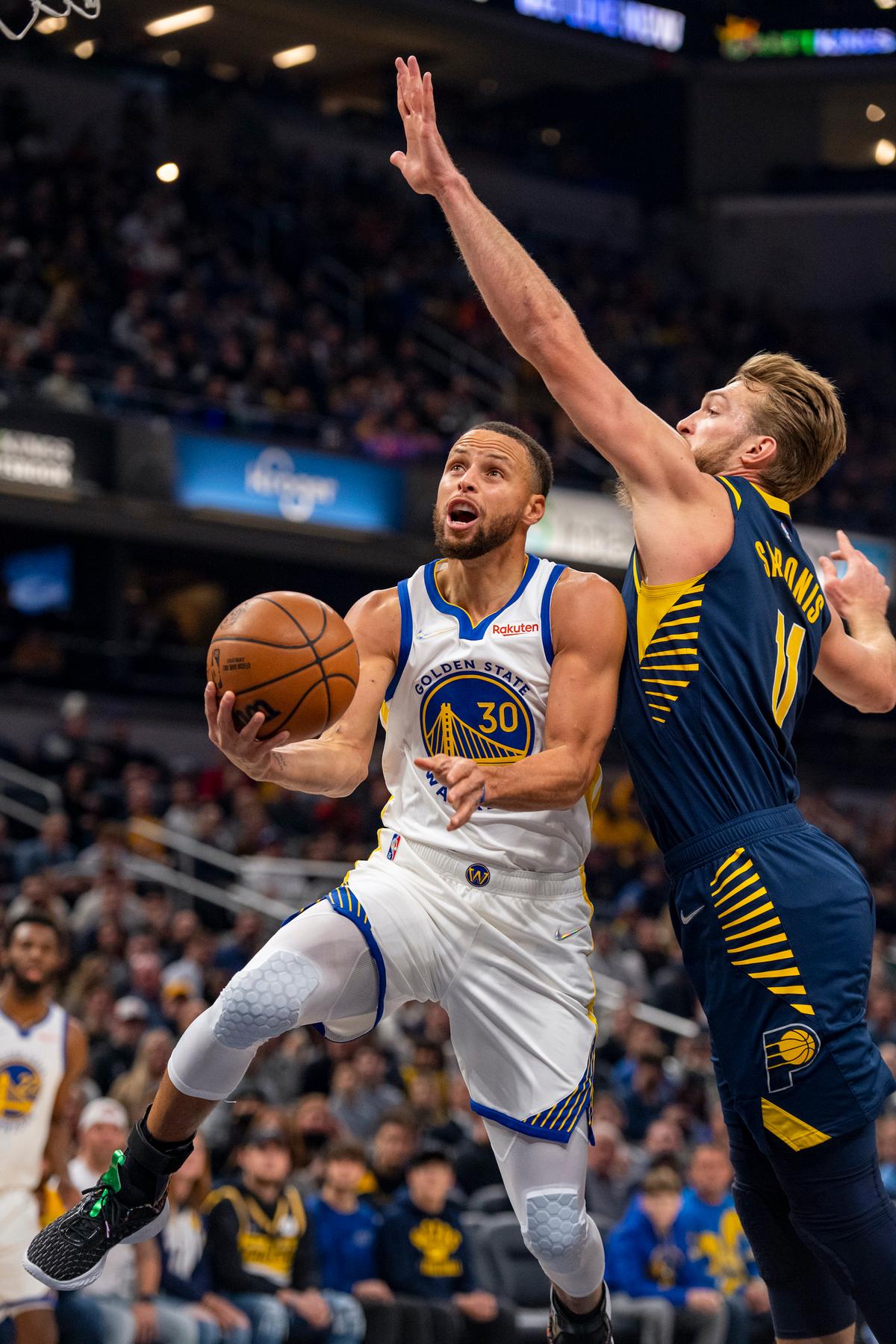 Golden State Warriors guard Stephen Curry (30) slips under the defense of Indiana Pacers forward Domantas Sabonis (11) for a scoring attempt during the first half of an NBA basketball game in Indianapolis, on Dec. 13, 2021. (Doug McSchooler/AP Photo)