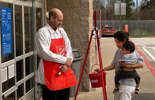 An unidentified woman with a child makes a donation to the Red Kettle drive of the Salvation Army of Tyler, Texas, as ringer Jeffrey Gordon give thanks and Christmas greetings. Dec. 14, 2021. (Patrick Butler/The Epoch Times)
