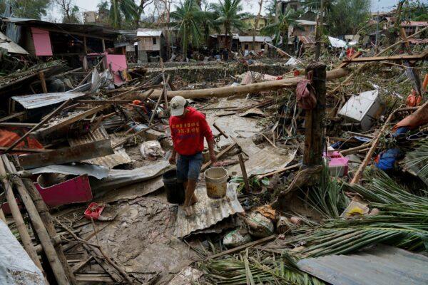 A man carries pails beside damaged homes due to Typhoon Rai in Talisay, Cebu Province, central Philippines, on Dec. 17, 2021. (Jay Labra/AP Photo)